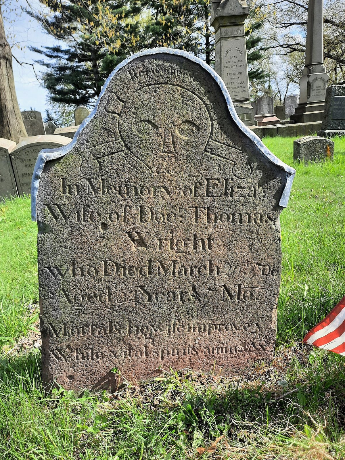 A weathered brown sandstone gravestone with a carved skull and crossbones under the word Remember, above an inscription for Eliza, wife of Doctor Thomas Wright