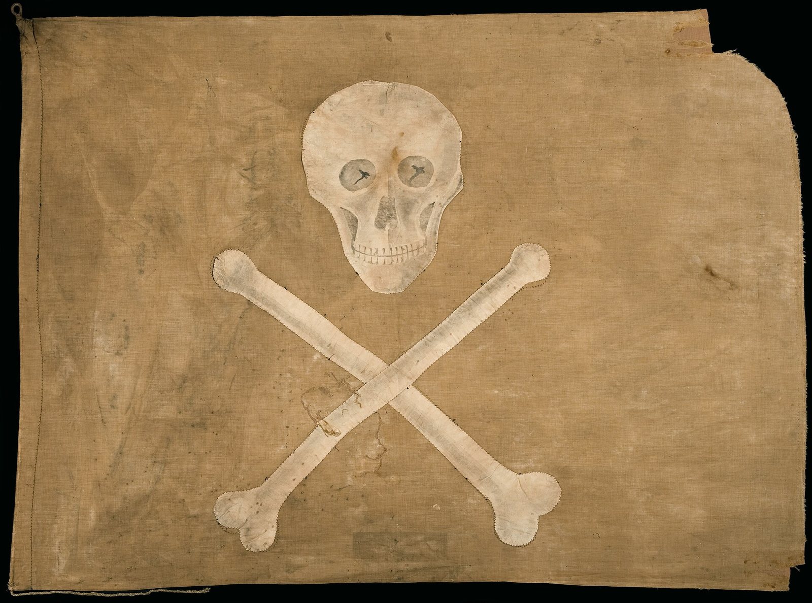 Una bandera pirata de algodón desteñida, con una calavera blanca sobre dos huesos cruzados, cosida sobre una tela marrón desgastada