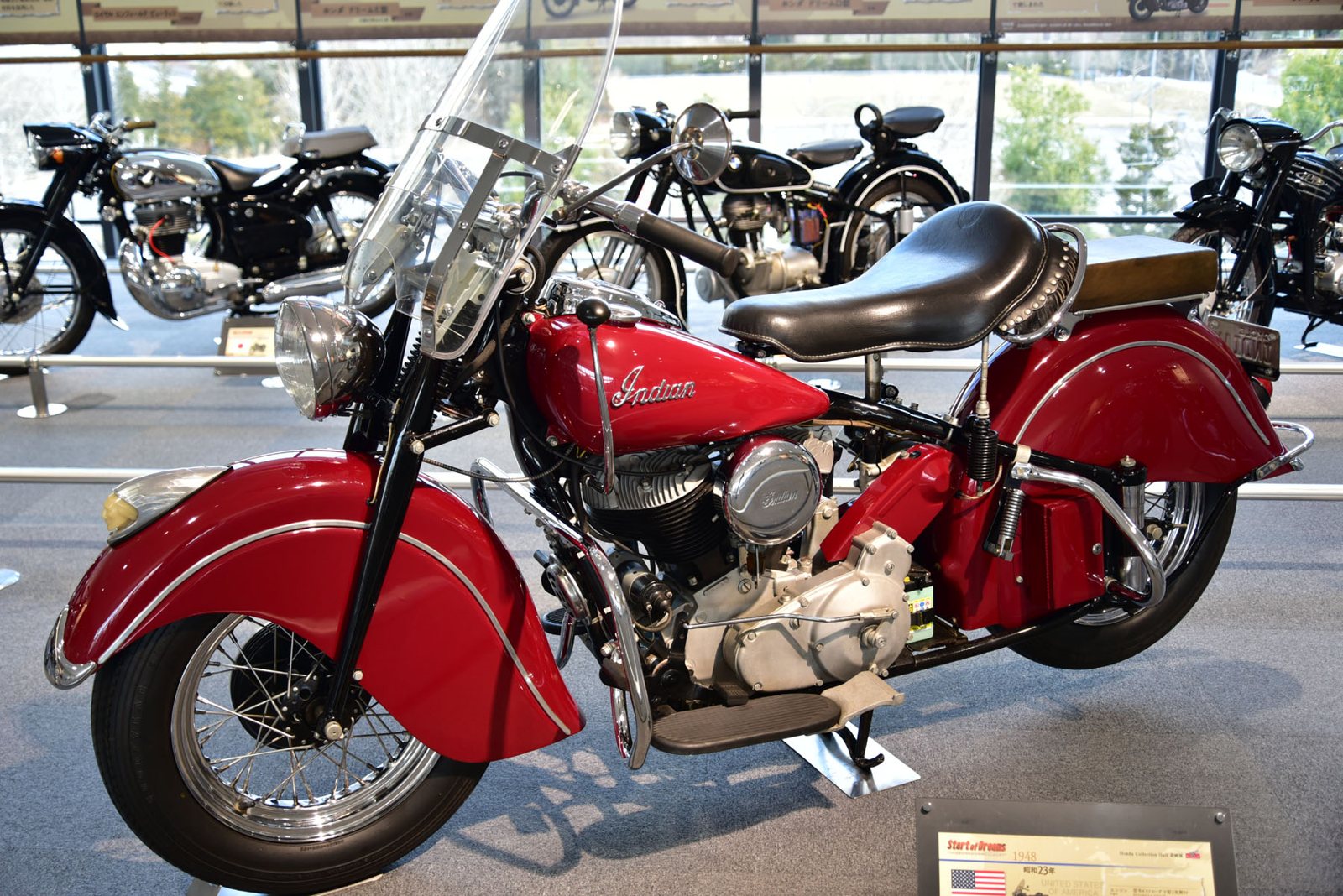 Una motocicleta Indian Chief roja de 1948, con parabrisas, asiento individual de cuero y guardabarros profundos, expuesta en un museo
