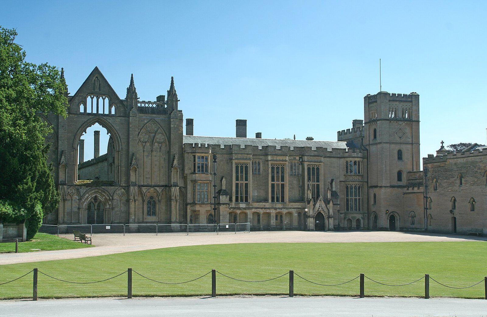 Newstead Abbey under a blue sky: the ruined Gothic west front of the priory church beside the battlemented house and tower, behind a wide lawn
