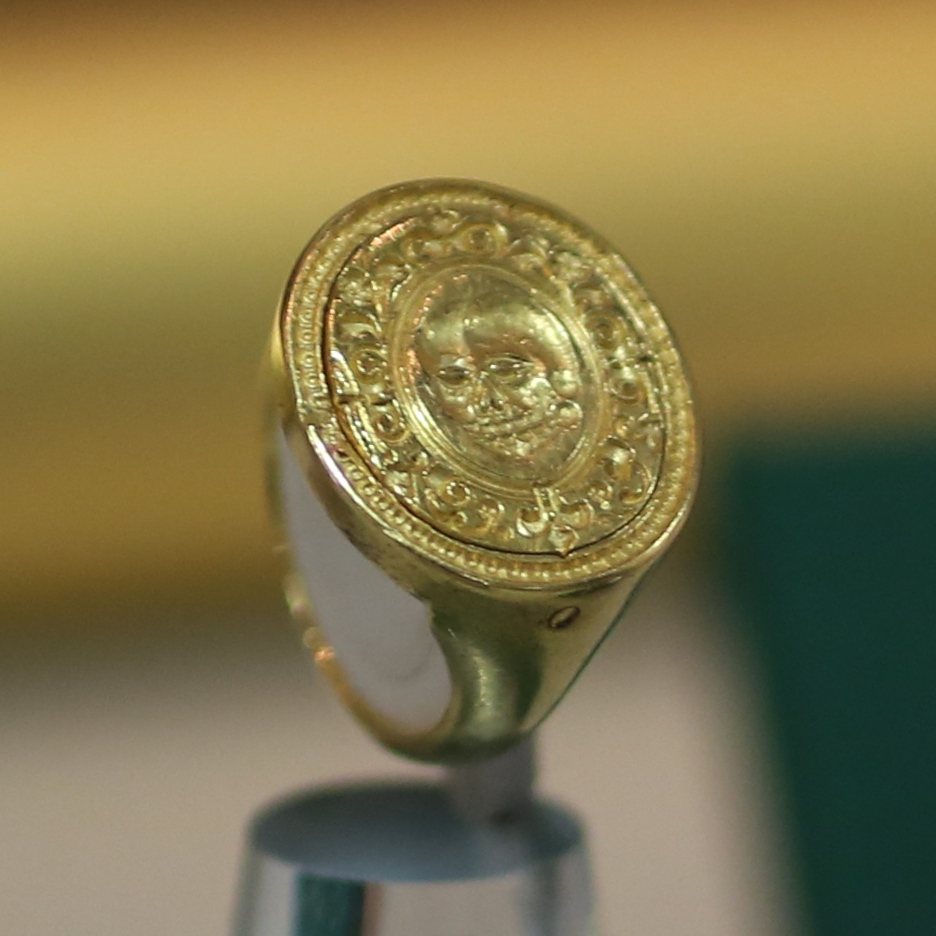 A gold signet-style ring with an oval bezel engraved with a skull and decorative border