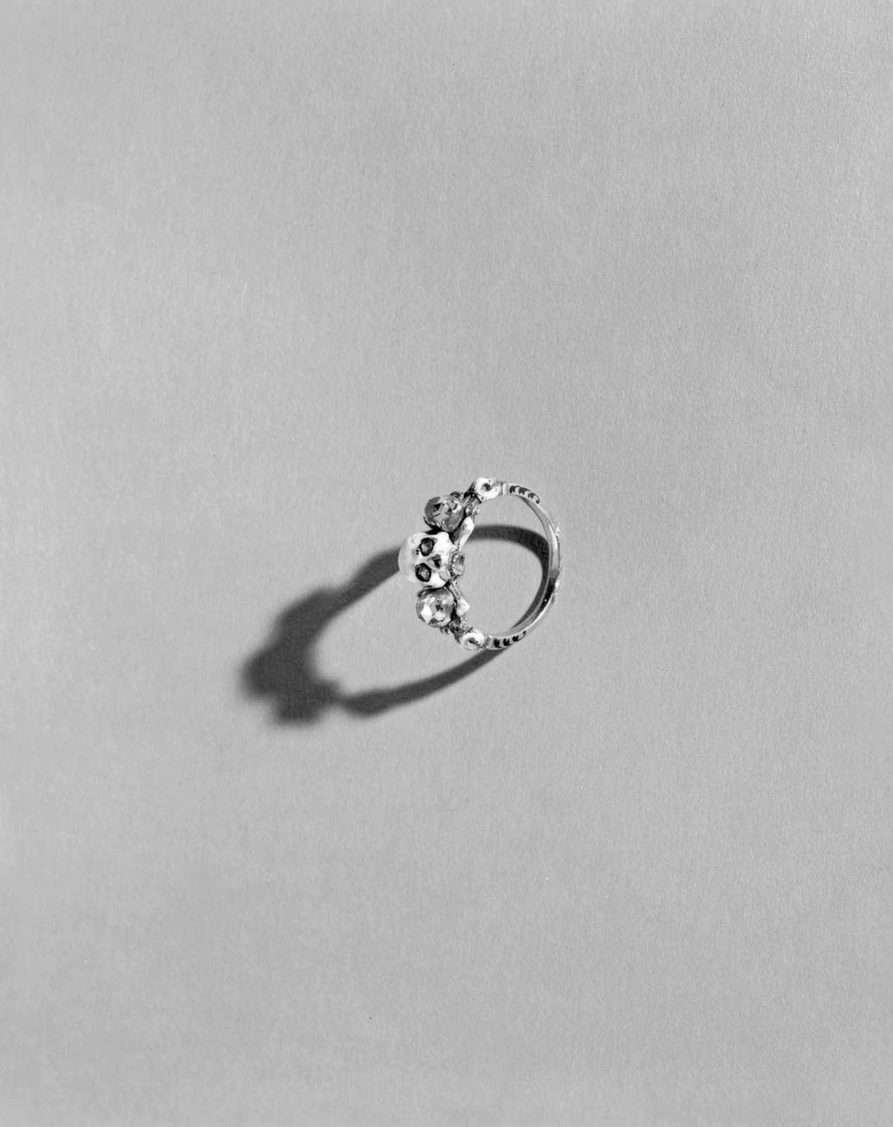 A small enamelled ring set with diamonds, casting a shadow on a grey ground