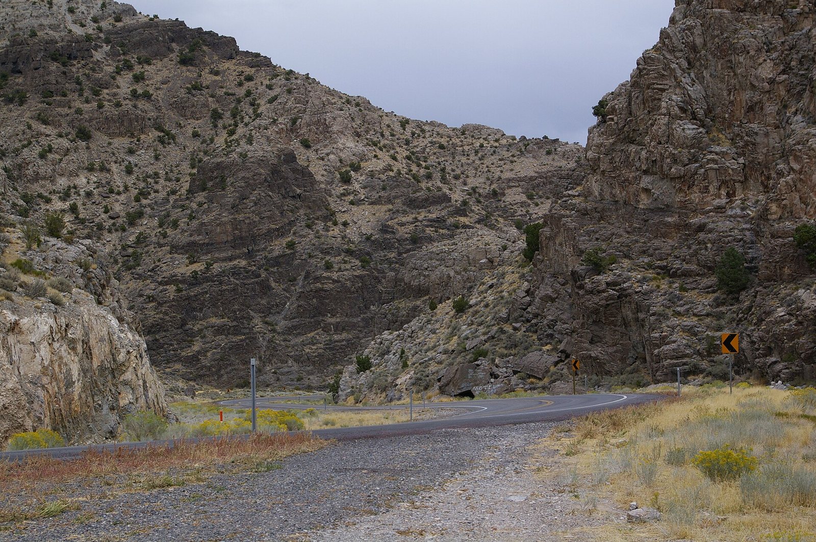 A road curving down through a narrow gap between brown rocky hillsides in western Utah, with desert scrub along the verge