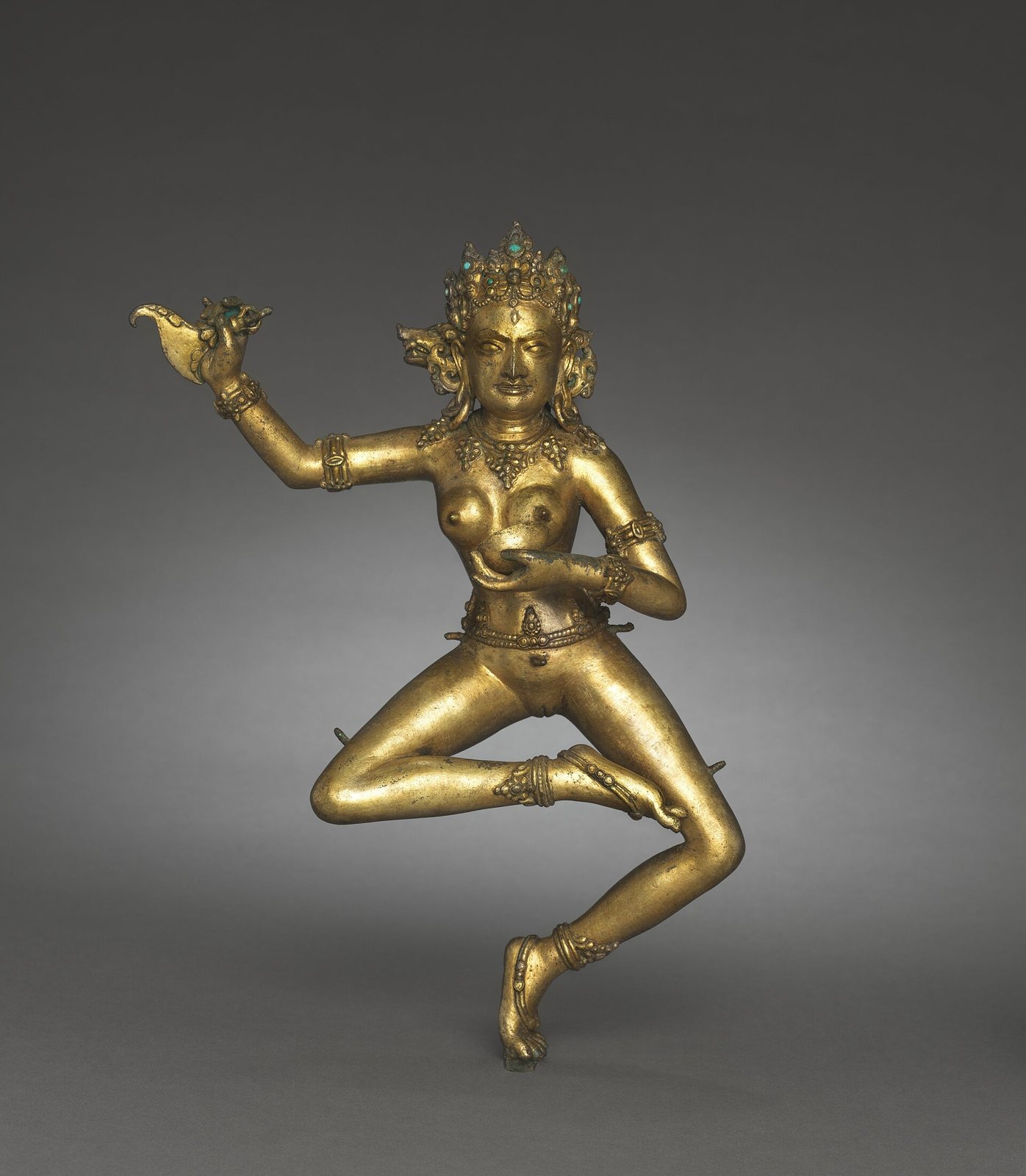 A gilt bronze figure of the goddess Vajravarahi dancing on one leg, wearing a tall crown and jewelled ornaments, one arm raised and the other holding a cup at her chest
