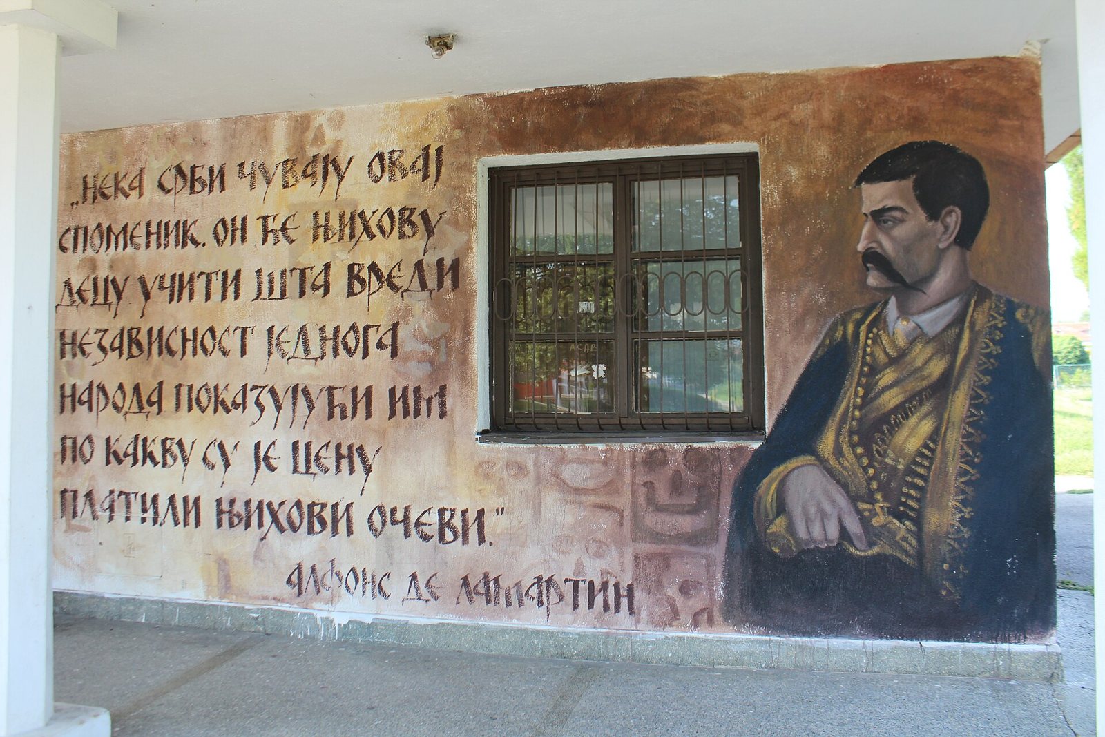A mural on an outside wall at the Skull Tower site: a Serbian quotation in Cyrillic signed Alphonse de Lamartine, beside a painted portrait of a man in a dark jacket