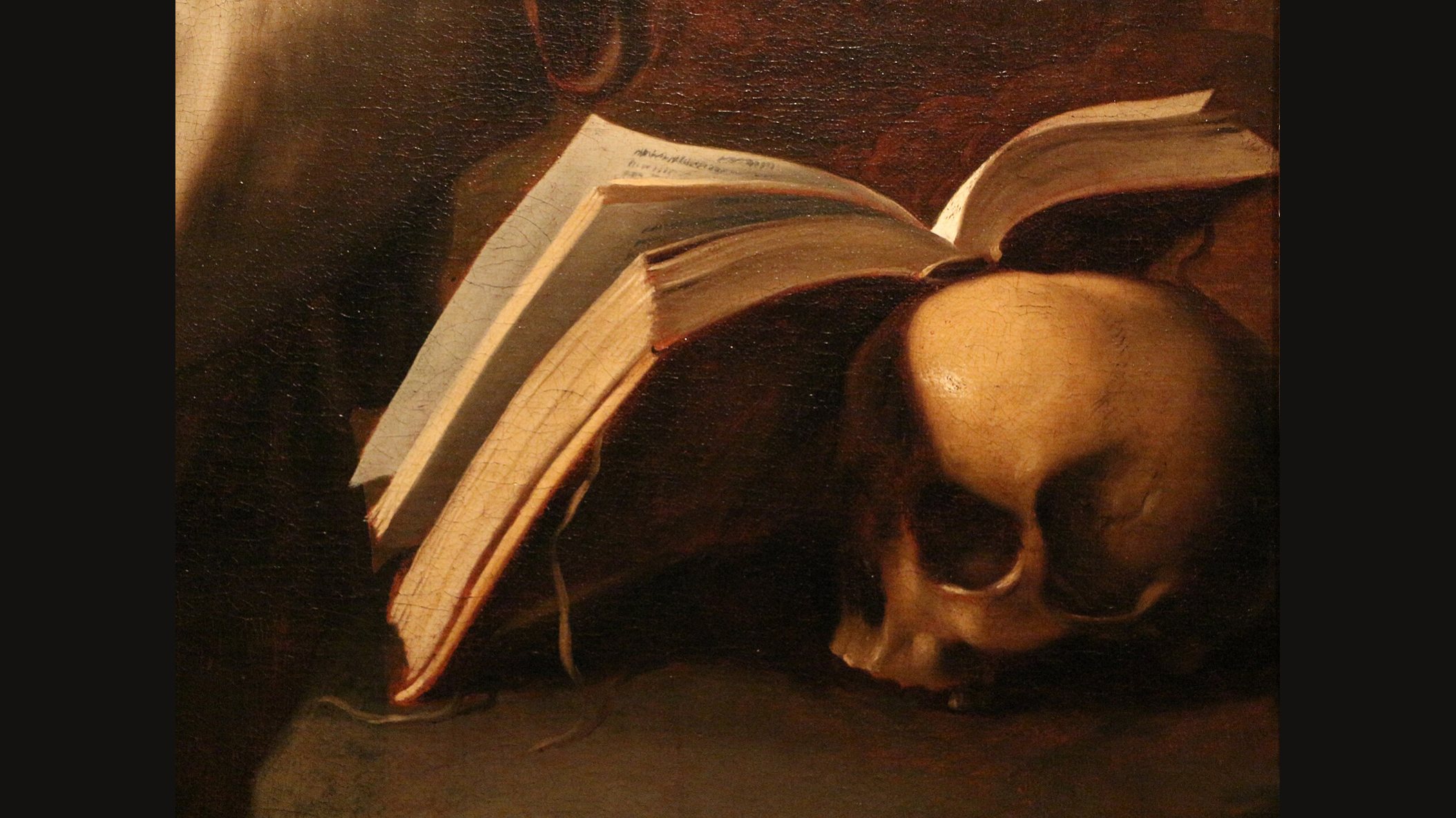 A human skull resting beside an open book in warm lamplight, a detail from Zurbarán's painting of Saint Francis in meditation