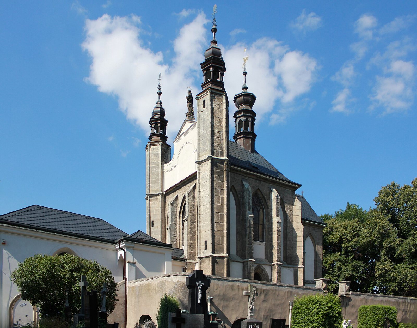 The white Gothic chapel of the Sedlec Ossuary in Kutná Hora seen from the cemetery under a blue sky
