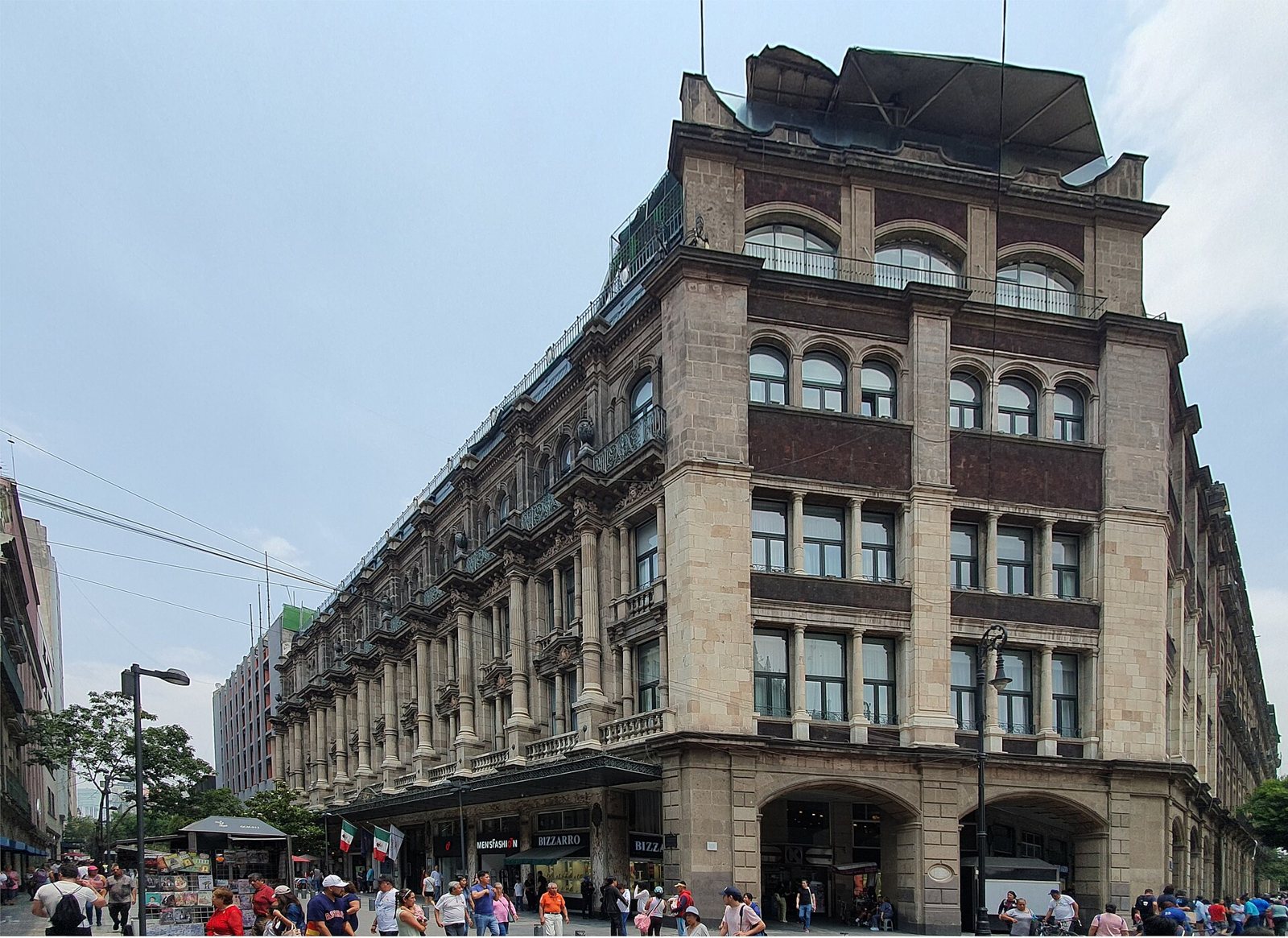 The corner of the Gran Hotel Ciudad de México, a six-storey stone building with arched windows, balconies and a glass roof, above a busy pedestrian street