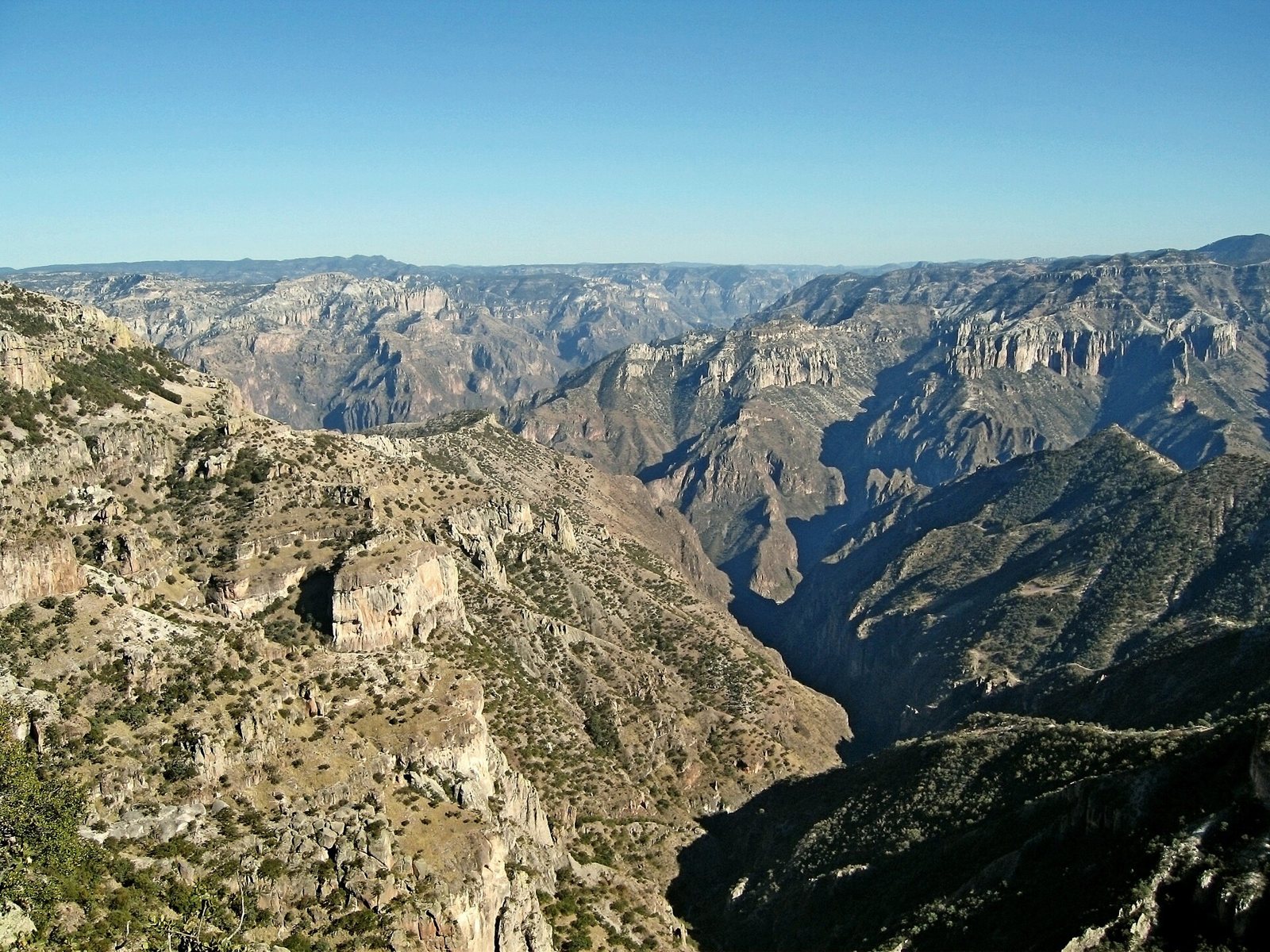 View over the rugged Copper Canyon in northern Mexico: dry rocky slopes in the foreground, a deep gorge below and a wide plateau on the horizon