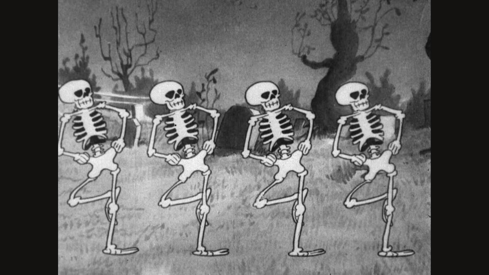 A black-and-white frame from the 1929 cartoon: four skeletons in a row dancing on one leg in a graveyard, with gravestones and bare trees behind them