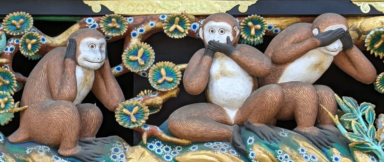 Painted wooden carving of three monkeys on a branch: one covers its ears, one its mouth and one its eyes
