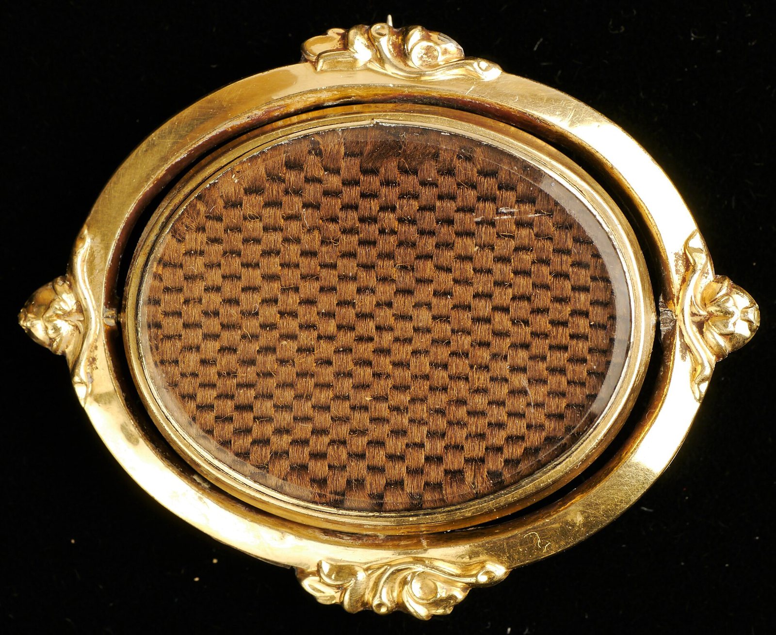 An oval gold brooch with a woven basketweave panel of brown hair under glass