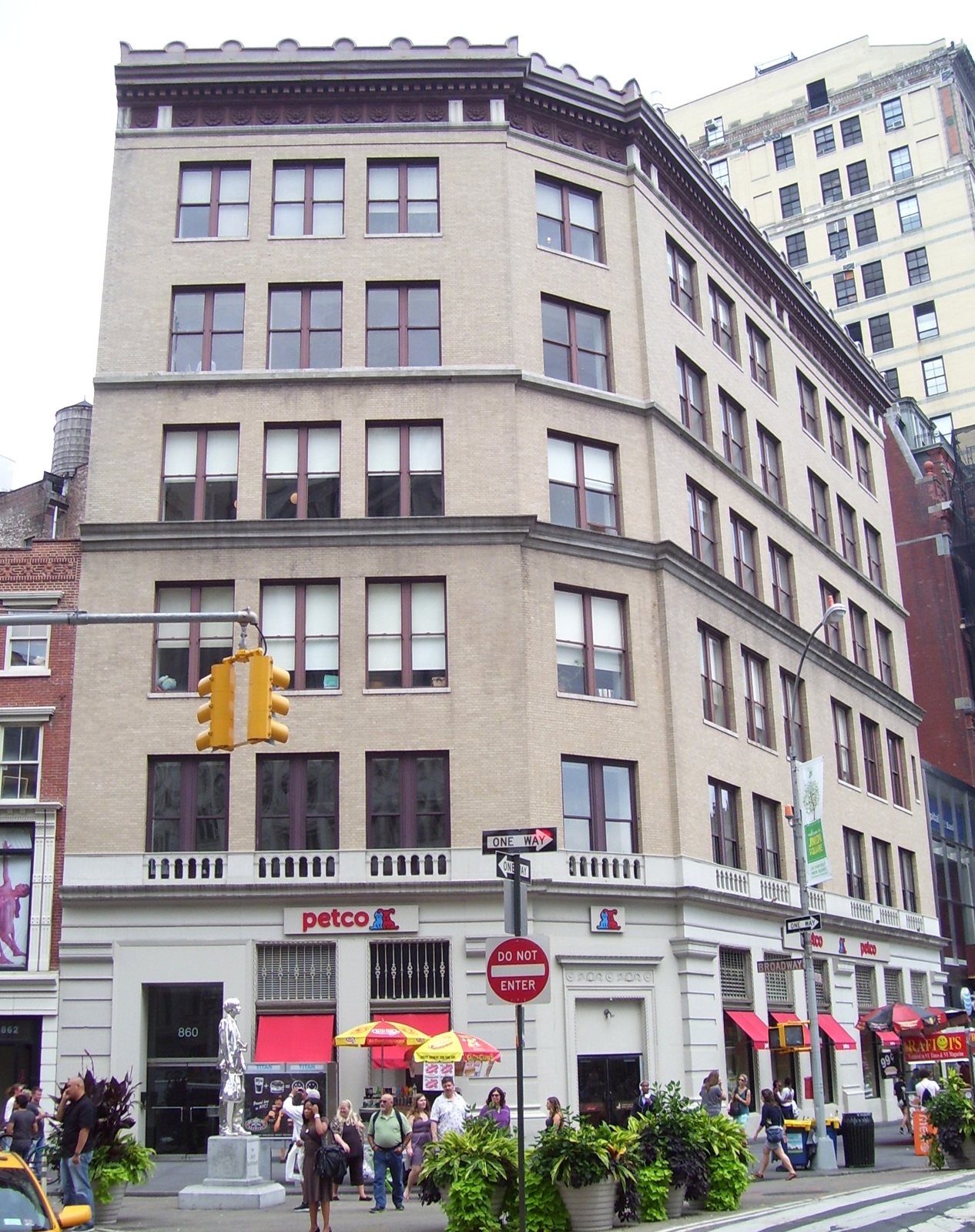 The corner of 860 Broadway on Union Square in New York, a tan stone commercial building of about ten floors, with shops and a crowded sidewalk at street level
