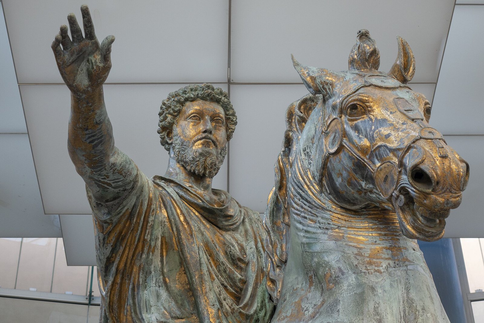 Vista cercana de la estatua ecuestre de bronce dorado de Marco Aurelio, el emperador barbado con un brazo en alto junto a la cabeza de su caballo