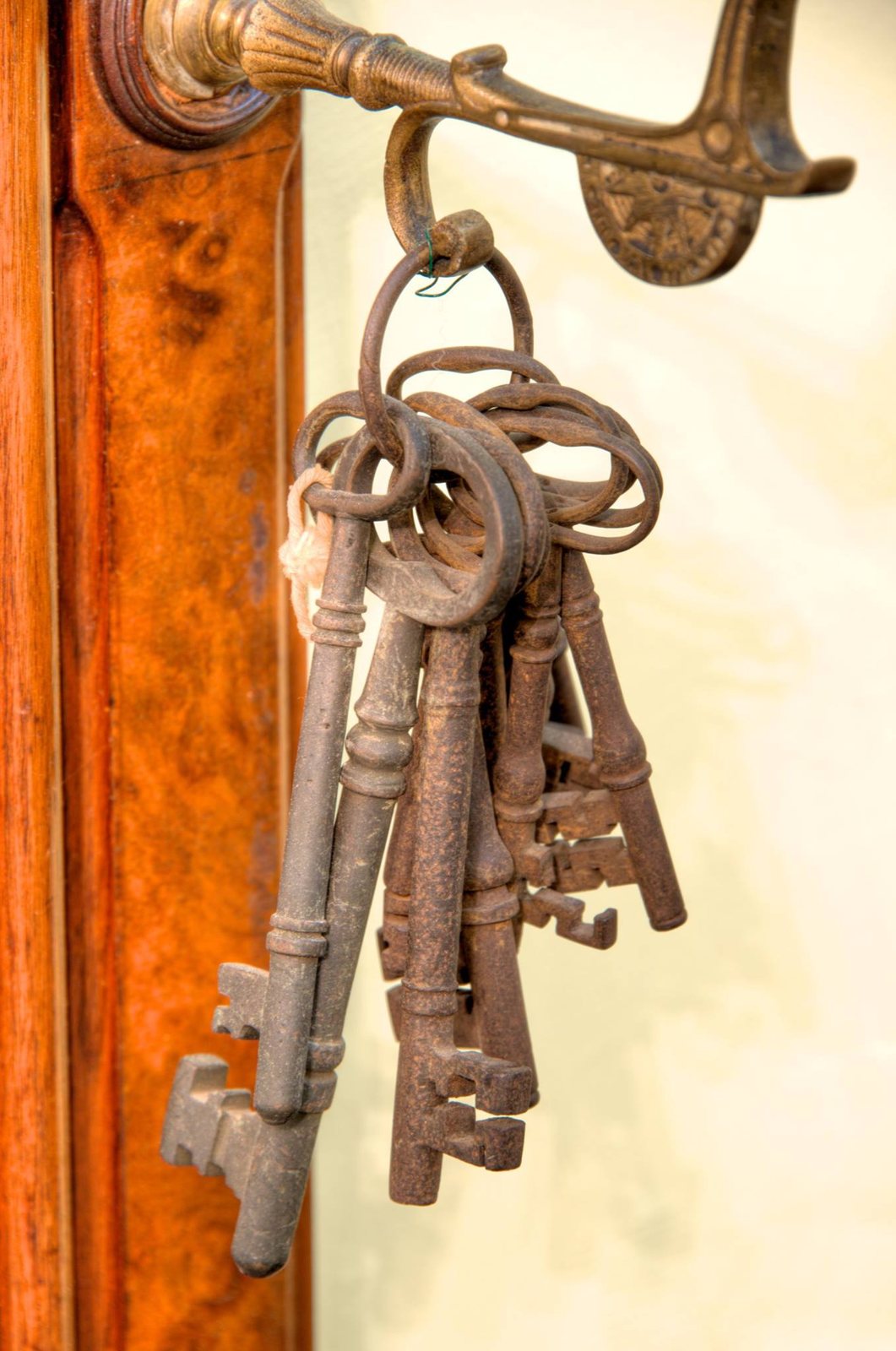 A bunch of old iron keys of different sizes on a ring hanging from a brass hook on a polished wooden door frame