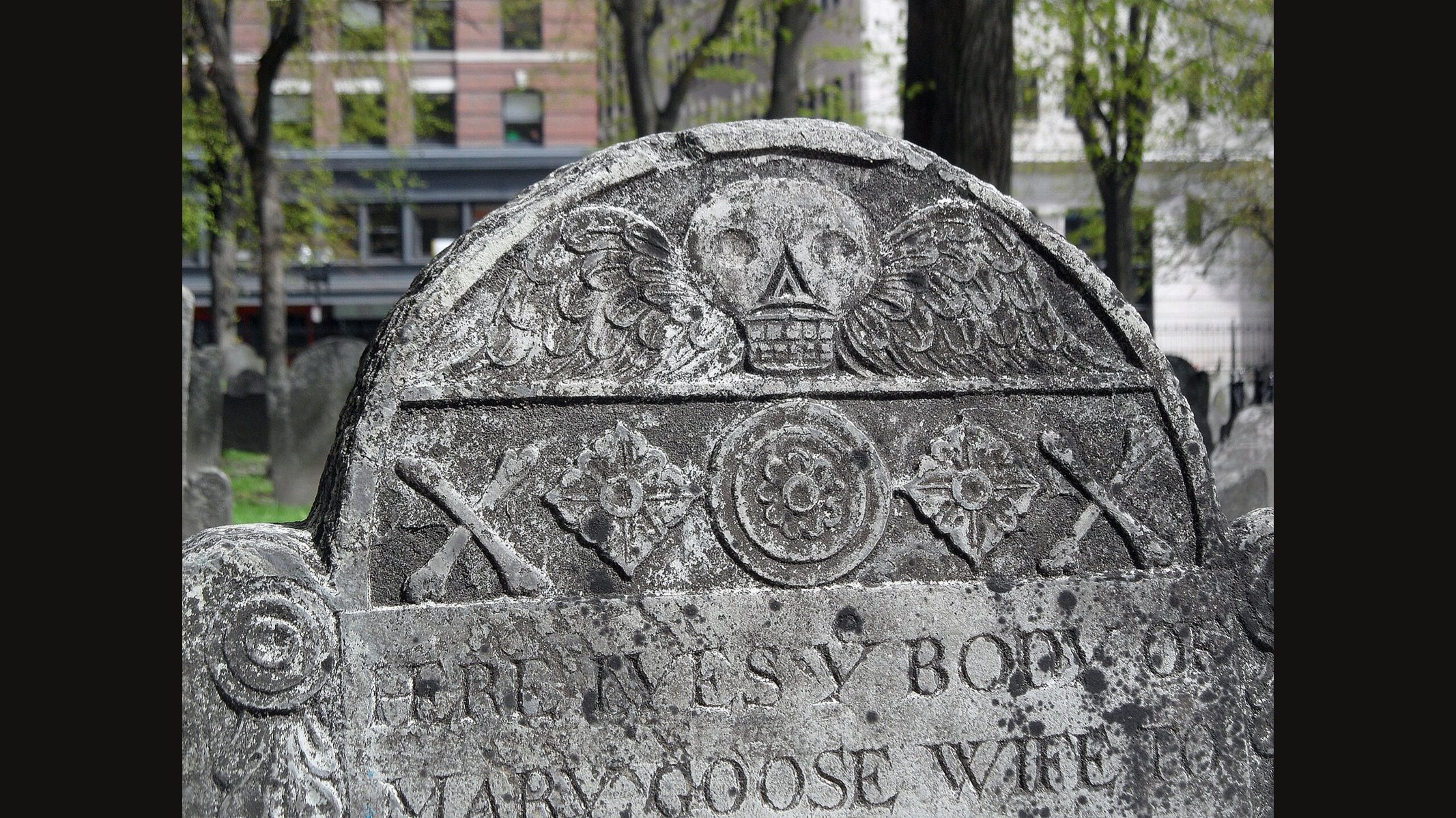 The top of Mary Goose's slate gravestone in Boston's Granary Burying Ground: a winged skull above carved rosettes and crossed bones
